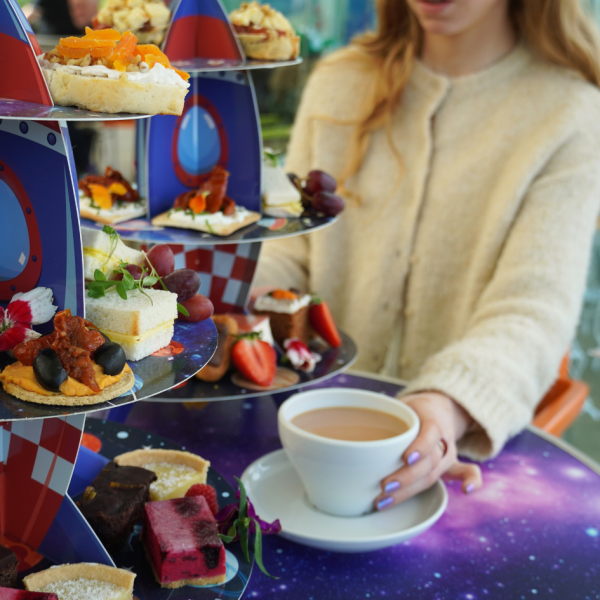 Person holding cup of tea next to afternoon tea stand.