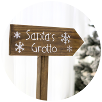 Wooden sign with "Santa's Grotto" painted on it in front of Christmas trees.