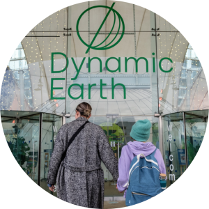 Parent and child holding hands walking towards Dynamic Earth entrance doors.